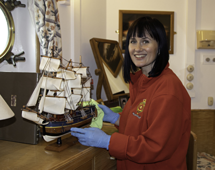 A woman member of the Housekeeping team dusting a model ship. 
