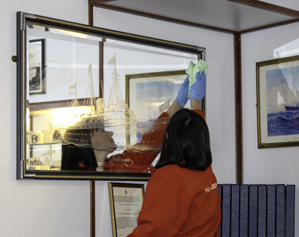 Housekeeper stands polishing a large mirror. 