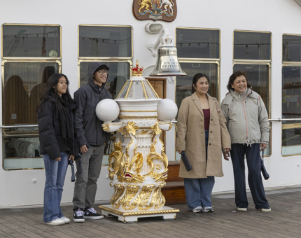A group of four people posing for a photograph by the Britannia Bell on the Verandah Deck. 