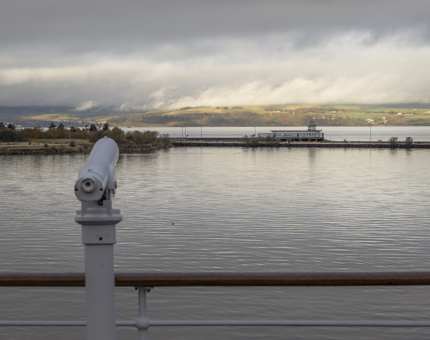 A telescope on the deck pointing out over the waterfront to the hills in the background.