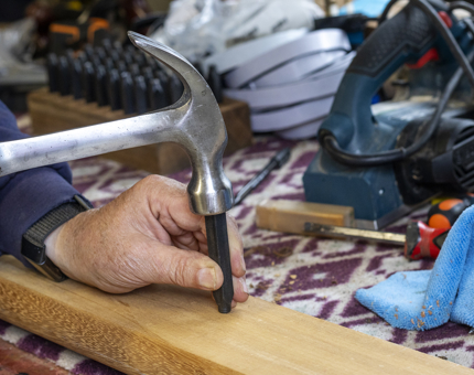 A close-up of a hand holding a hammer, marking up a handrail.