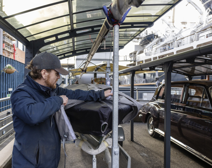 A member of the Maintenance team placing a cover over Coweslip, a small sailing boat.