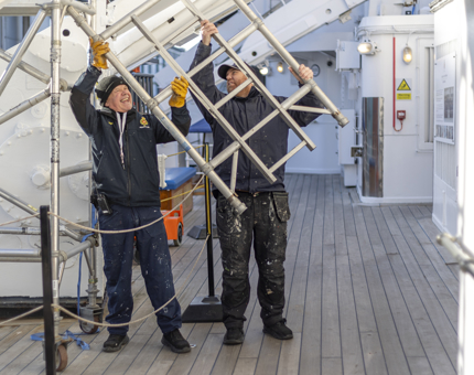Two maintenance team members putting up scaffolding on the Port Shelter Deck for painting work.