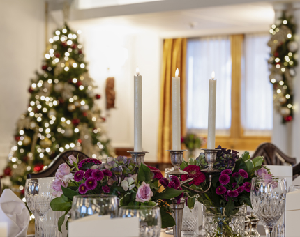 Table settings in the State Dining Room. There is a candelabra on the table with a Christmas tree in the background. 