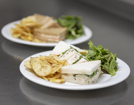 Two plates of sandwiches with crisps and salad. 