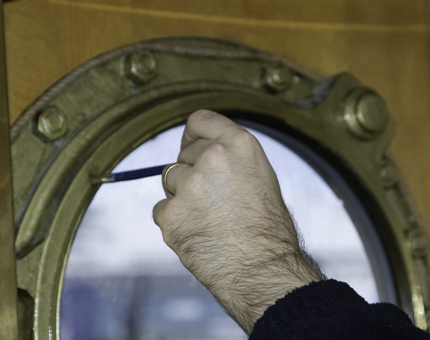 A man is holding a paintbrush and painting a porthole on Fingal. 