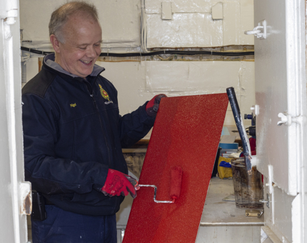 A man from the Maintenance team is painting a stair tread with red paint. 