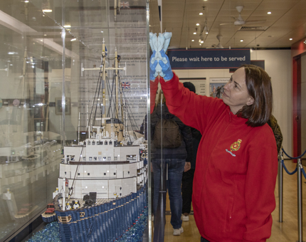 A woman Housekeeper polishing a display case containing a LEGO model of Britannia. 