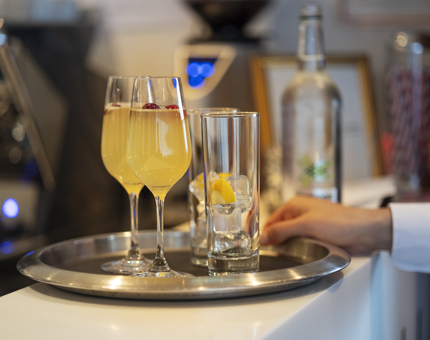 A tray on drinks, including two mimosas. There is a hand resting on the tray. 