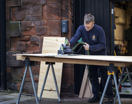Maintenance team member cutting wood for storage aboard Fingal Hotel.