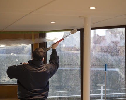 A Ceiling being painted white with a paint roller by a Maintenance man. 