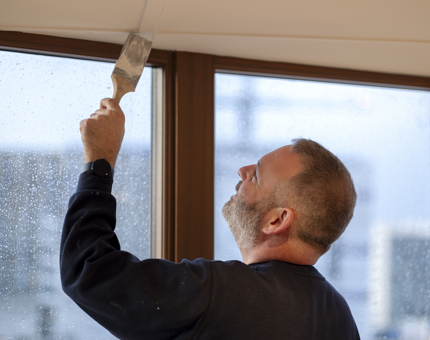 A man holding a paintbrush painting a ceiling white.
