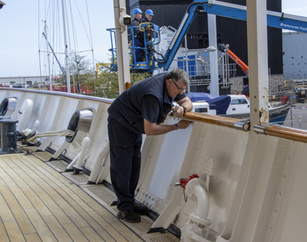 A man from Maintenance is working on a handrail on deck. 