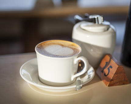 A cup of coffee with a saucer and teaspoon sitting on a table.