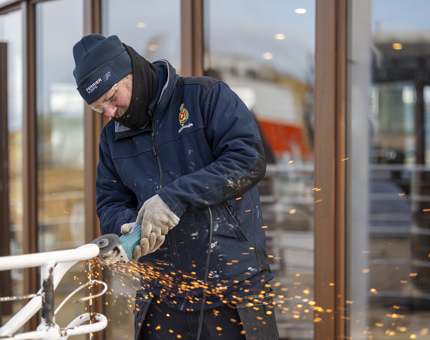 A Maintenance team member preparing handrails by using a grinder to remove the paint.