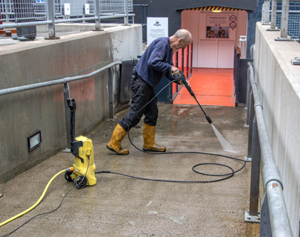 A man from the Facilities team is washing down the entrance to the Engine Room with a power washer.