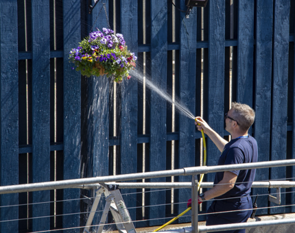 A man is watering hanging baskets on the Quayside. 