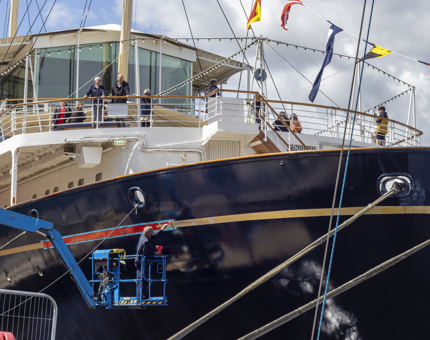 A man on a cherrypicker is preparing the ship's hull for the gold leaf application.