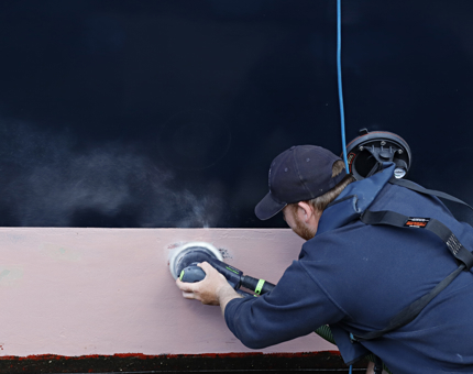 A member of the Maintenance Team is sanding the hull.