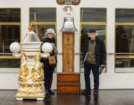 Two visitors pose for a photo at The Royal Yacht Britannia's Bell and binnacle on the Verandah Deck. 
