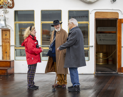 Three people stand on the Verandah Deck talking. 