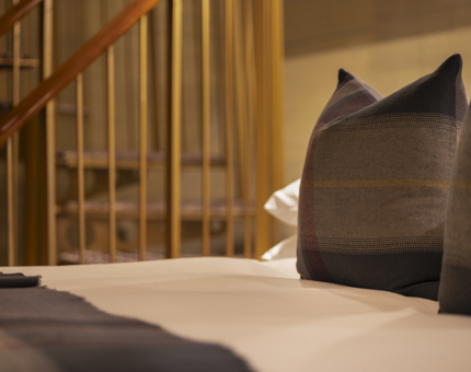 A Close-up of a bed in one of Fingal's cabins. The bed had a white duvet cover with tartan blanket and pillows.