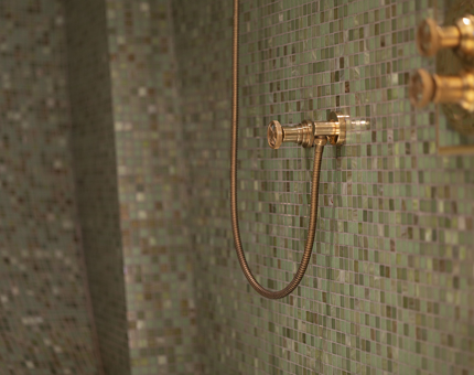 A green tiled shower with brass fittings.