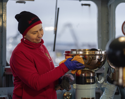A Housekeeper wearing a red fleece polishing brass components in Britannia's Bridge.