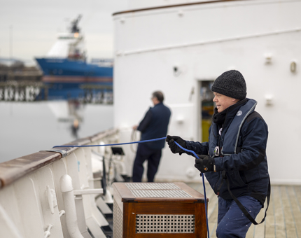 Two Maintenance men pulling blue ropes that are attached to the paint cat. They are moving it into position out of shot. 