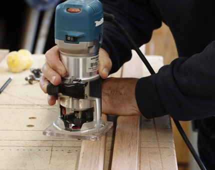 A close up of a hand holding a cutting machine, cutting lengths of wood to make picture frames.