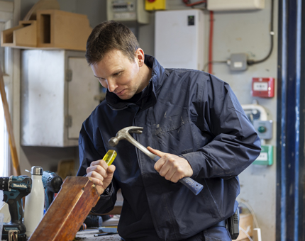 A man holding a hammer and chisel. He is fixing a perry buoy and lantern stand.