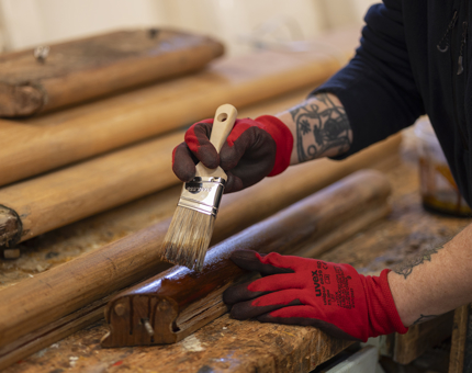 A pile of handrails being varnished. There is a man wearing red gloves holding a paintbrush.
