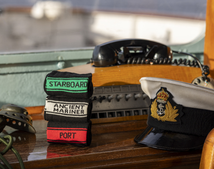 Three pairs of socks are stacked on the bench in front of the phone in the Bridge. The socks have written on them Starboard, Ancient Mariner and Port. There is a Captain's hat sitting next to them. 