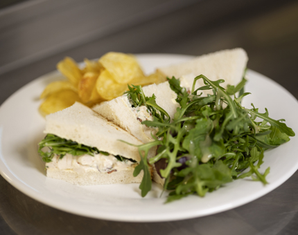 A chicken sandwich made on white bread. On the plate there are crisps and a salad. 