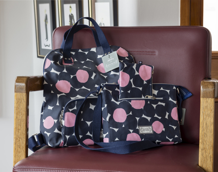 A selection of bags with a navy blue, pink and white flower print on them. They are sitting on a burgundy coloured chair. 