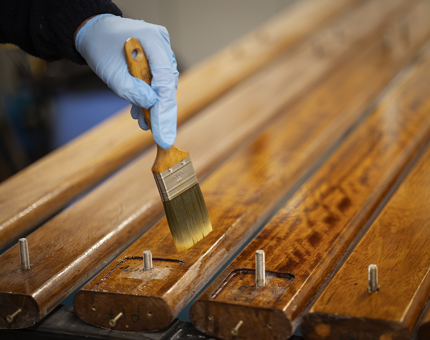 A close-up of a hand wearing a blue glove holding a paint brush, varnishing handrails.