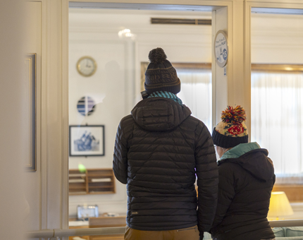 A view from behind two visitors listening to an audio guide handset looking in to the State Apartments. 
