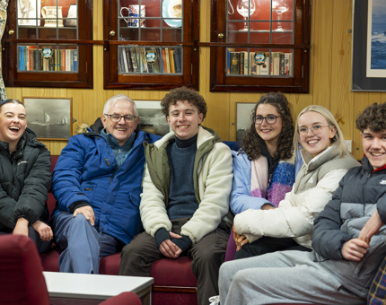 A group of 6 people are sitting on the seats in the Petty Officer's Mess. 