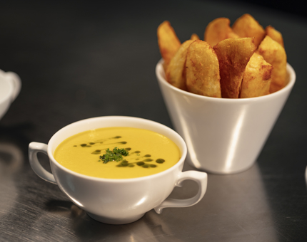 A bowl of butternut squash soup and a bowl of potato wedges. 