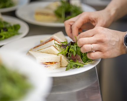 A close up of hands placing salad leaves on a plate of sandwiches. 