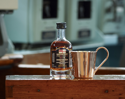 A bottle of Navy rum with a brass cup next to it.