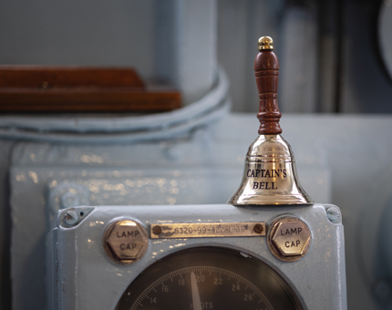 A Captain's Bell. It is silver in colour with a brown wooden handle.