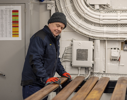 A man wearing a blue jacket, hat and red gloves holding a paintbrush, varnishing wooden handrails. 