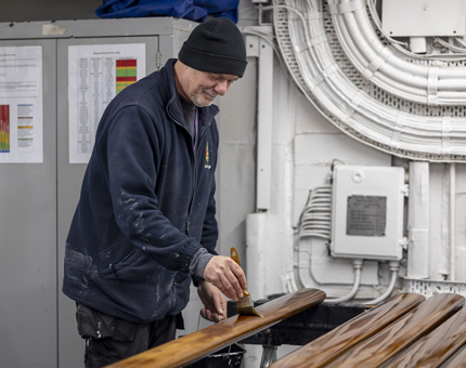 A Maintenance team member holding a paintbrush, varnishing handrails.