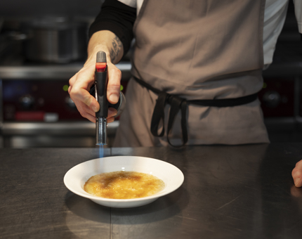 A Chef holds a blowtorch over a bowl of porridge, heating up the whisky sugar on top. 