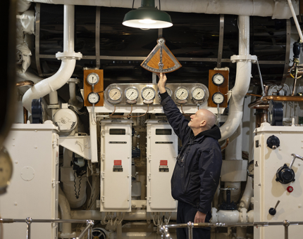 A maintenance team member is reaching up his arm to check the clinometer in the Engine Room.