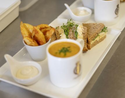 A plate with a mug of soup, egg sandwich and potato wedges.