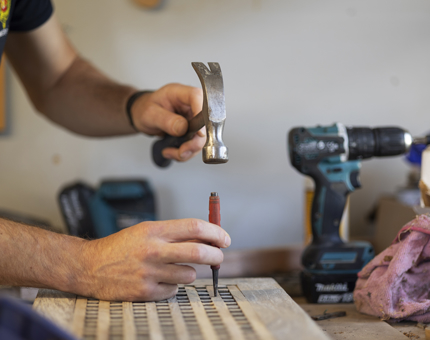 A close up of hands holding a hammer and tool to remove wooden slats. 
