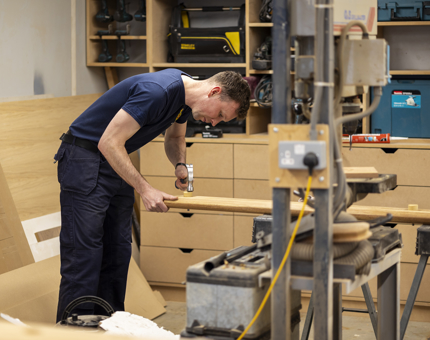 A Maintenance team member hammering a wooden screw into the handrail. 
