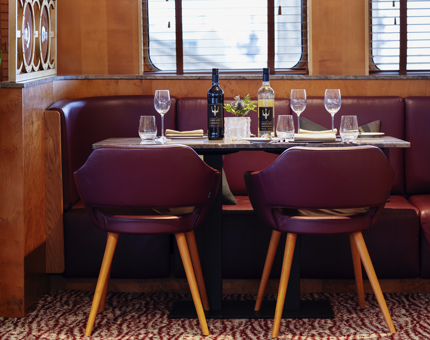 A dining table in The Lighthouse Restaurant. There are bottles of wine and glasses on the table. The chairs are purple leather.